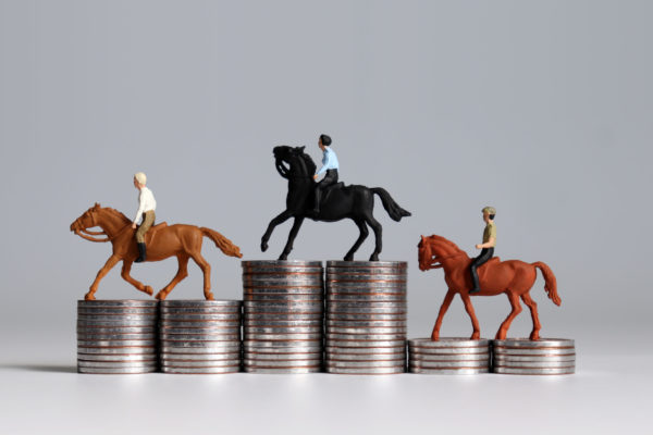 Three miniature men riding horses on piles of coins. Three pile